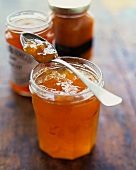 Open Jar of Homemade Peach Jam with a Spoon; Jars of Jam