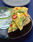 Three Slices of a Vegetable Frittata on a Plate with a Glass of Ice Water