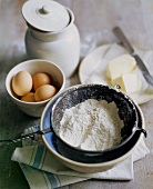 Mehl in einem Sieb, Eier und Butter