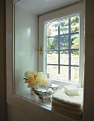 A handtowel with soap, bathing utensils and flowers on a window sill