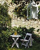 Weisser Klapptisch und Klappstuhl zwischen blühenden Gartenblumen vor rustikaler Natursteinmauer