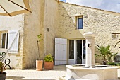 Gepflasterter Hof eines südländischen Steinhauses mit Steinbrunnen und mediterranen Pflanzen in Terrakottavasen