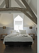 A white bedroom with a double bed in an attic with visible beams