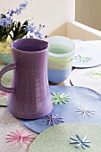 A purple water jug and a stack of bowls on place mats decorated with stars