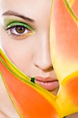 A young woman with green make-up peeking out from behind a plant