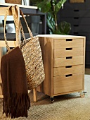 Rolling file cabinet out of wood with drawers and shopping basket hanging on a chair