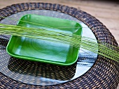 Grüne Schale mit Ziergräsern auf Glasplatte eines Rattantisches