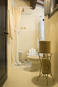 Offene Tür mit Blick ins Bad auf Beistelltisch mit Körben und Dusche mit weißem Vorhang