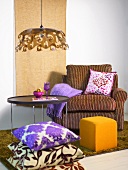 Cozy reading chair with a yellow upholstered foot stool and stack of pillows in front of a side table