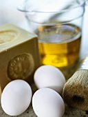 Three white chicken eggs in front of a bar of soap and a filled measuring jug