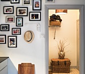 A collection of pictures hanging on the wall and a view into an illuminated hallway with a basket in front of the door