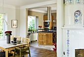 A dining area and an old tiled stove in front of an open-plan kitchen with a view of a counter