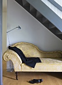 A chaise longue under a flight of stairs with a jacket on it and a pair of shoes under it