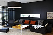 A black wall with a narrow window and a wooden lattice wall in a living room furnished with black chairs and a sofa and a wooden coffee table