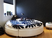 A corner of bedroom - a round bed with a flower pattern on the bed clothes against a black wall