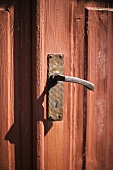 An old red, wooden door with a handmade metal handle