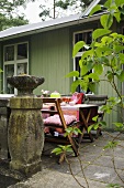 A table laid on a stone terrance in front of a green, wooden house