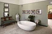 Free standing bath tub in front of a gray wall on a stone floor and antique bench