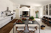 Kitchen with eating area -- plates with vegetables on a gray metal table and folding wooden chairs with white upholstery on a white tile floor