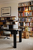 Black table in front of a illuminated book shelves in a wall niche and wall shelving in 50's style