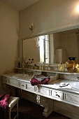 Wenig beleuchteter Waschtisch mit Badutensilien auf Marmorablage und Wandspiegel
