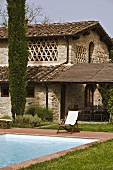 Lounge chair beside a pool in front of a Mediterranean house and a covered terrace