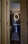 Open door with a view into a bathroom with a white pedestal sink with a lighted mirror