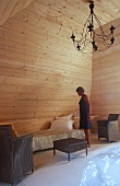 Frau steht im Wohnraum eines hohen Dachraums, Wand und Decke sind mit hellem Holz vertäfelt