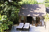 Haus auf den Malediven - im Innenhof stehen vor dem Palmenhäuschen zwei Liegestühle mit weissen Polstern