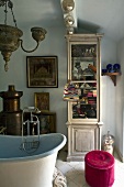 Corner of an oriental style bathroom with pink ottoman and glass fronted cabinet