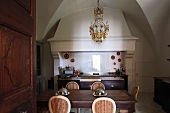 Blick auf Esstisch vor altem Küchenofen mit Abzug und Kronleuchter unter Gewölbedecke