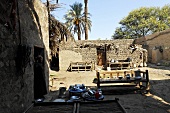 Lehmhäuser und Bänke auf Sandboden im Innenhof und hochgewachsenen Palmen, Ägypten