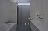 Half-darkened bathroom in designer style -- vanity top with recessed sink and built-in cabinets with plinth lighting