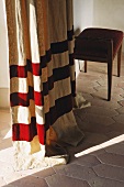Floor length curtain with red stripes and stool on a terracotta floor