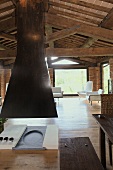 Offener Kamin mit schwarzem Abzug unter der Holzbalkendecke eines renovierten Landhauses