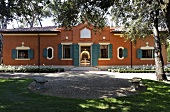 A villa with a red brick facade and blue shutters in a garden with a gravel path