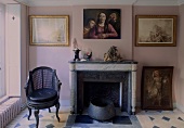 Sitting room with a fireplace in an old building with paintings on a pink wall and patterned floor tile
