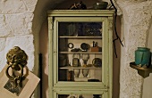 Green glass front cabinet with antiques in front of a rustic wall
