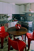 Round wooden table with red plastic chairs in a built-in kitchen