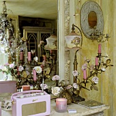 A gilded candle holder, an antique table lamp and a pink portable radio in front of a wall mirror