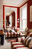 Wohnraum in einer Villa mit rot weiss gestreiftem Zweisitzer vor raumhohem Spiegel mit Lichterkette vor roter Wand