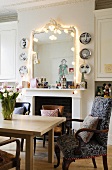 A dining area in front of a white fireplace and a mirror with a chain of light