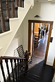 An old stairway - dark wooden banisters and floor boards with a view through an open doorway into a living room