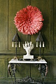 Coral-coloured wall decoration on a dark wood-panelled wall and black metal table lamps a white bust on a marble top wall table