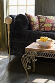 A dark plush sofa with cushions and a filligree occasional table with a bowl on it