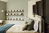 A double bed in front of a wooden paravent and geometric figures on a shelf in front of a grey wall