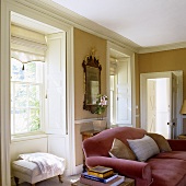 A red sofa in the living room of a county house in front of a window with interior shutters