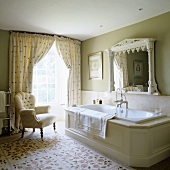 A spacious, traditional English country house-style bathroom with floor-to-ceiling windows and a comfortable armchair