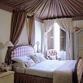 A bedroom in a traditional English country house - a fabric-covered ceiling and a bed with a small canopy