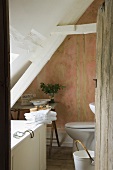 An open wooden door with a view into a partially renovated attic bathroom in an old country house